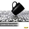 GANT09_50 Schwarze Tasse auf einer Anti-Ermüdungsmatte mit schwarz-weißem Ornament-Muster.